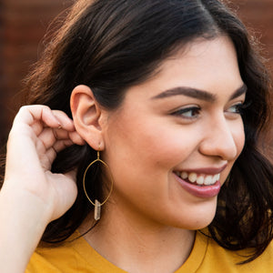 Model is wearing crystal quartz oval hoop earrings. Made from nickel free metal. Approximately 3.5 inches long from earring hook to bottom of crystal.
