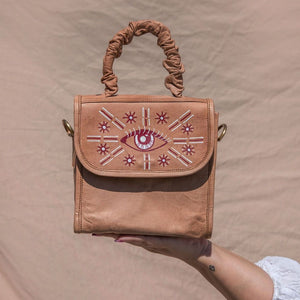 Brown leather purse with Third eye painting on front flap. A scrunchie handle and crossbody strap. Height is 7.5 inches,  Length is 7.5 inches, Width is 5 inches.