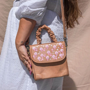 Brown leather purse with pink mushroom painting on front strap. With a scrunchie handle and a crossbody strap. Height is 7.5 inches,  Length is 7.5 inches, Width is 5 inches.