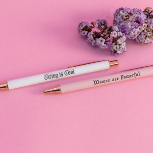 Womxn Are Powerful Pen set comes with (2) luxurious writing pens One white pen (Caring Is Cool) One pink pen (Womxn are Powerful) 