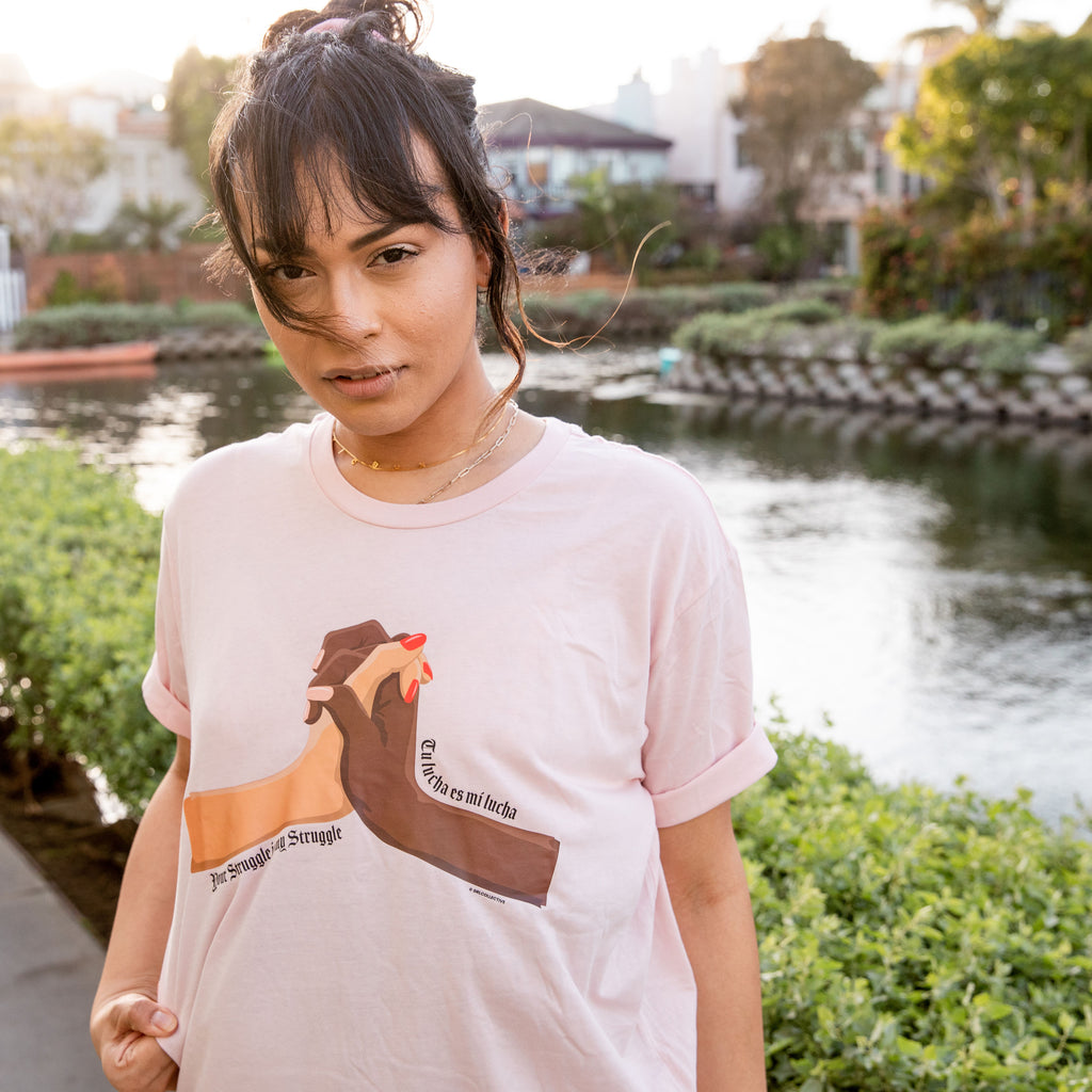 Model is wearing Your Struggle Is My Struggle/ Tu Lucha Es Mi Lucha Pink Tee. Unisex Tee fit, sizing from XS-4XL. Made of 100% cotton. 
